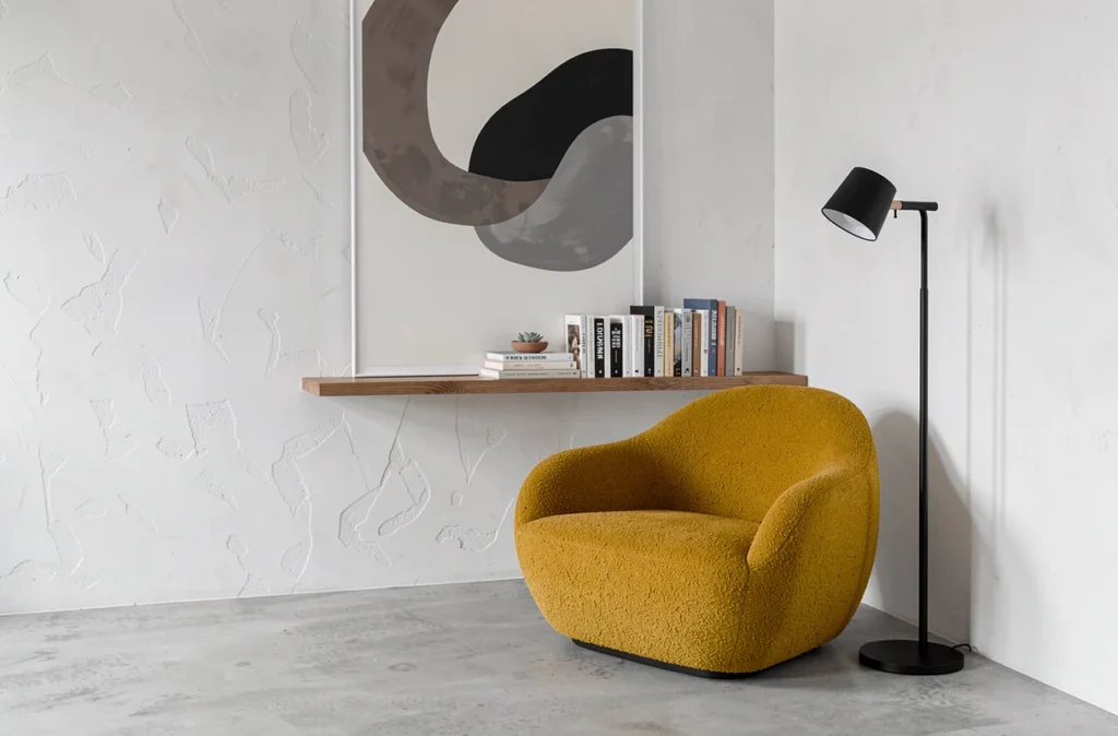 Coin lecture minimaliste de style scandinave avec fauteuil en bouclé moutarde, étagère flottante en bois et plante succulente sur fond de mur blanc